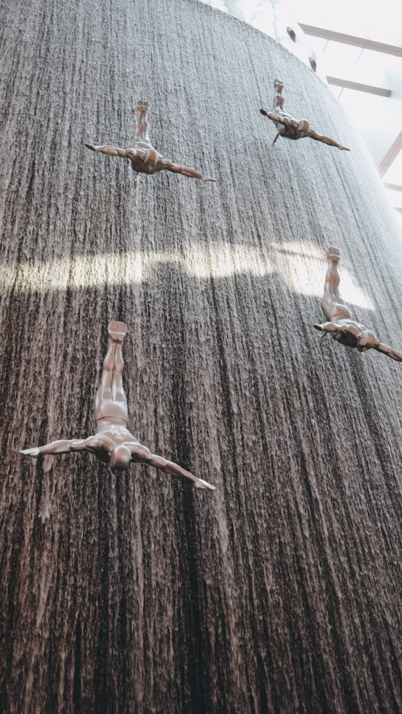 Artistic sculptures of divers in a stunning vertical waterfall display at Dubai Mall.