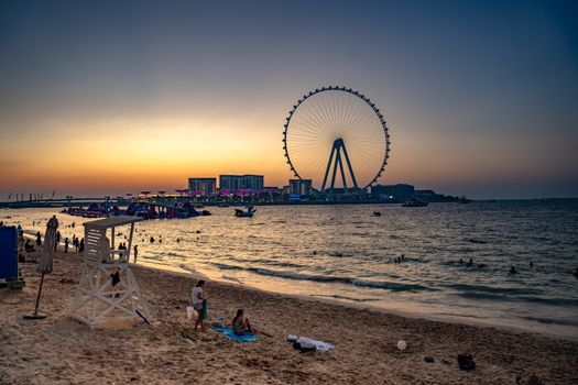 Serene sunset with Dubai Eye and beachgoers enjoying the evening by the water.