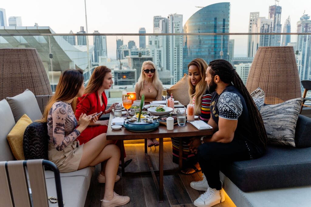 Group of friends dining on a rooftop terrace with a stunning view of Dubai skyline.