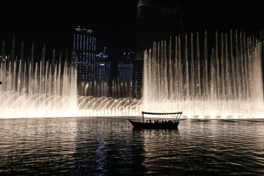Silhouette of a boat against the illuminated Dubai Fountain at night, showcasing the city skyline.